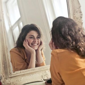 Woman-smiling-with-teeth-at-her-reflection-in-a-mirror,-proud-of-her-dental-health image
